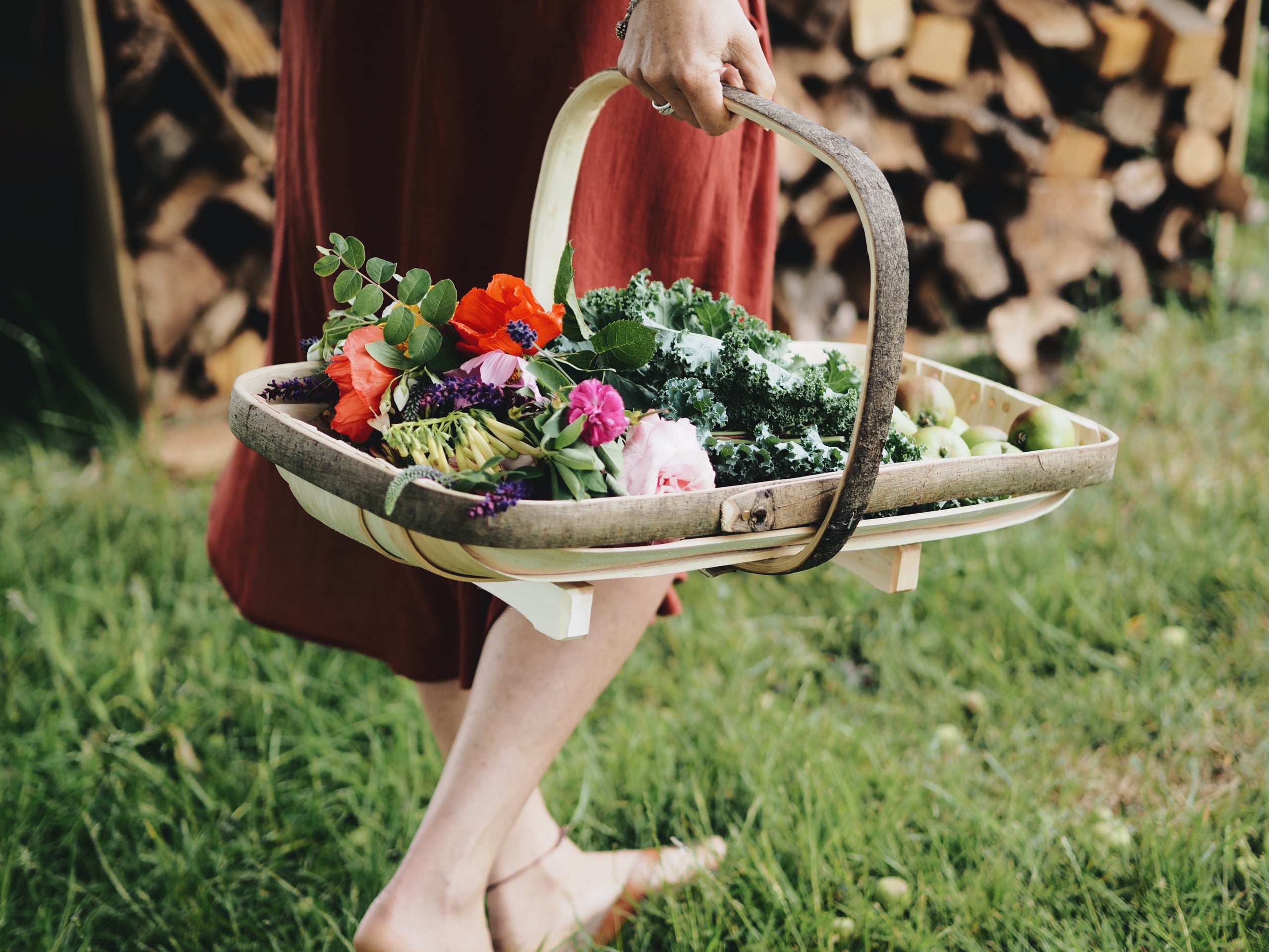 Person holding a basket of fresh vegetables and flowers in a natural setting