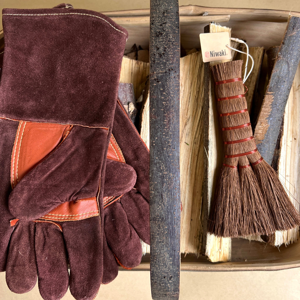 Pair of maroon leather gloves next to a Niwaki broom and Log Trug