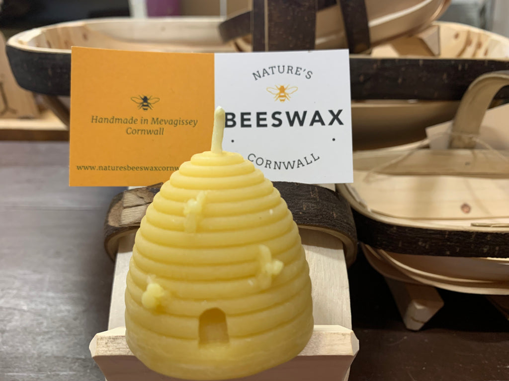A small beeswax skep candle with a brown and white label in front, displayed on a wooden stand.